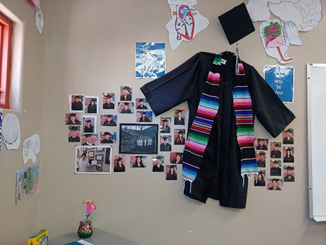 Graduation cap and gown stapled to the wall surrounded by pictures of students in their cap and gown